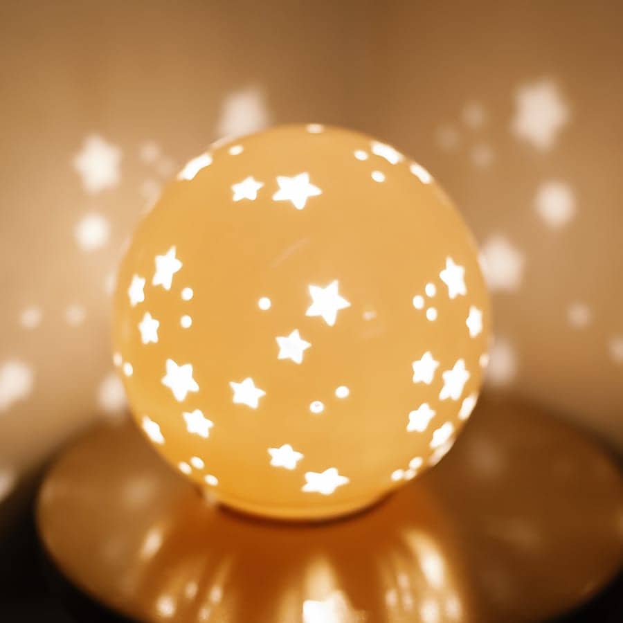 A round ceramic lamp glowing warmly, casting star shapes onto the wall behind it